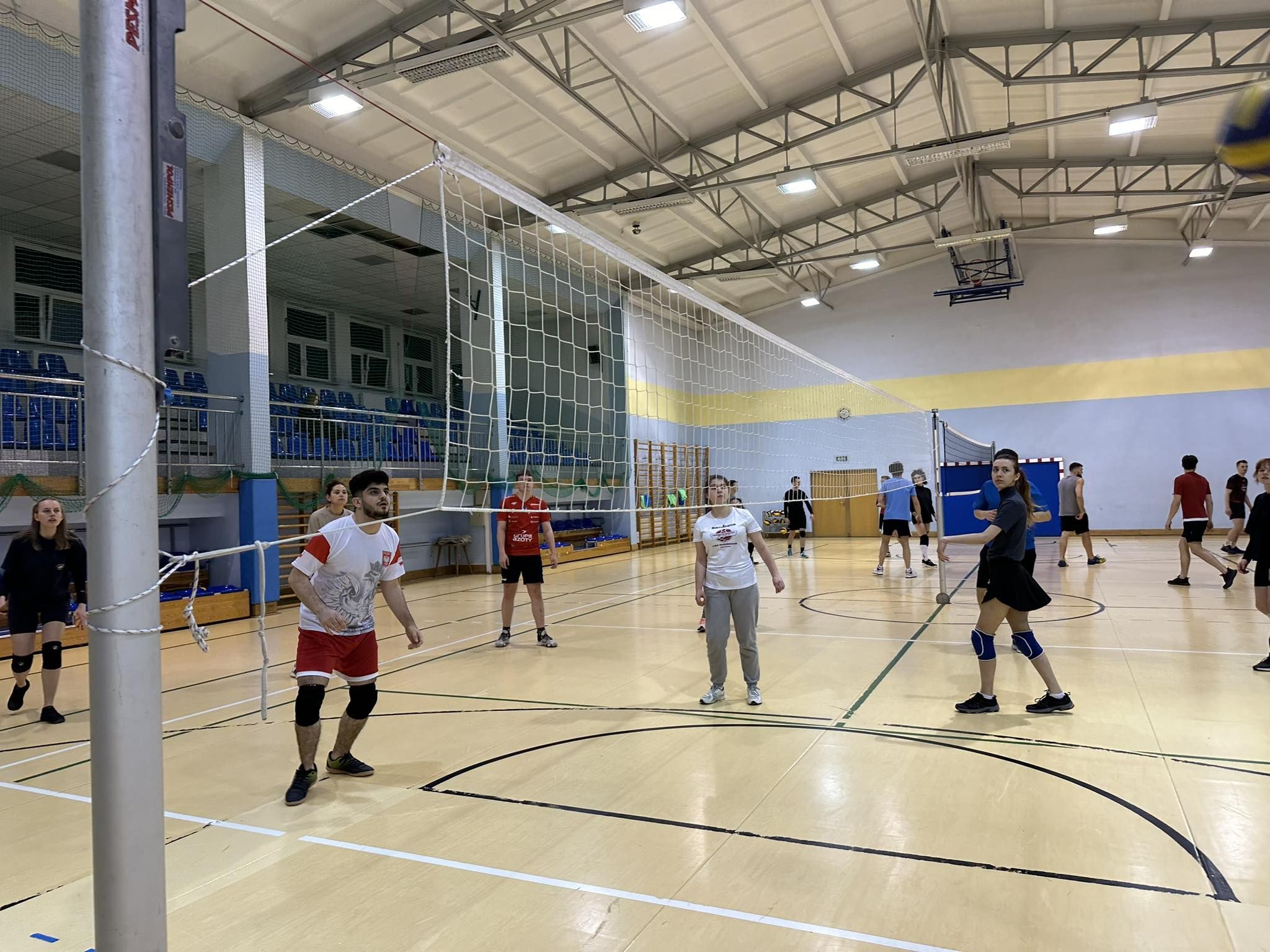 tudenci Erasmus+ biorą udział w zajęciach sportowych na sali gimnastycznej, grając w siatkówkę.